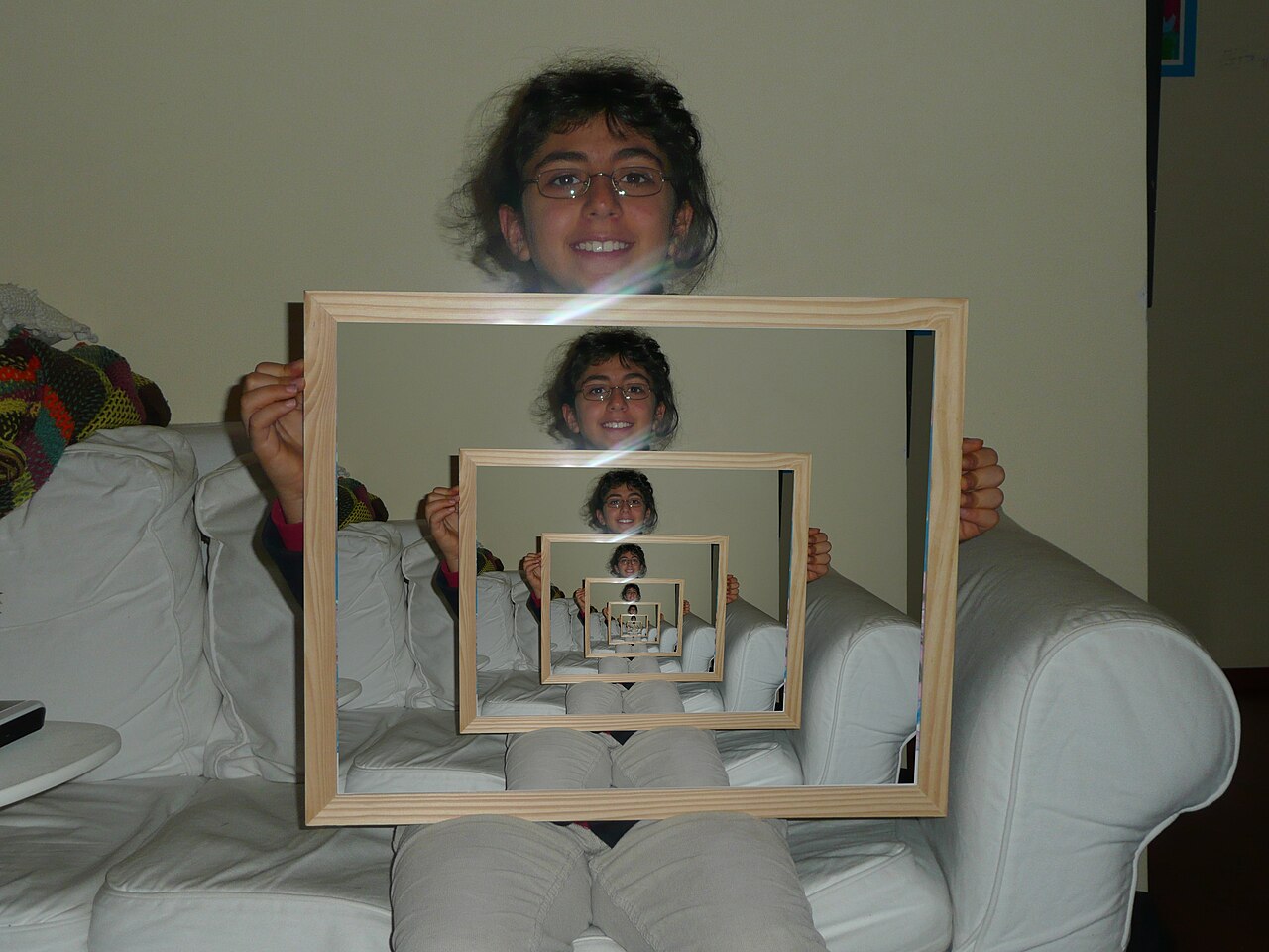 A photograph of a person holding a picture frame; inside the frame is the same person holding the same frame, repeating into the distance.